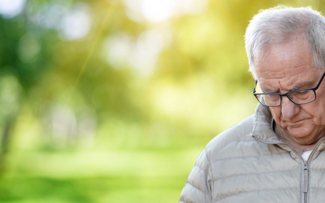 Elderly man in a grey duffle coat stood in a green outdoor space